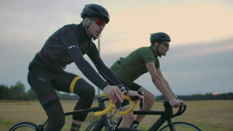 Two-cyclists-ride-on-the-road-in-the-evening-after-sunset.-Early-morning-training-cyclists-in-helmets